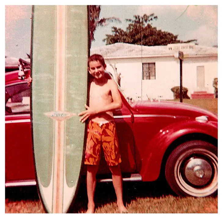 Boy with surfboard and red car.